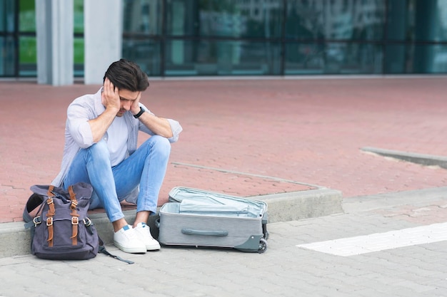 Mixed Up Luggage Desperate man sitting near airport terminal with suitcase