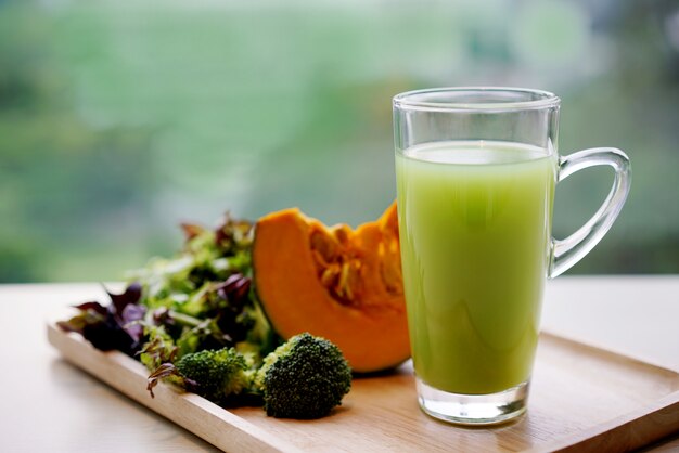 Mixed vegetable juice in glass and fresh pumpkin, broccoli and vegetable on wooden tray.