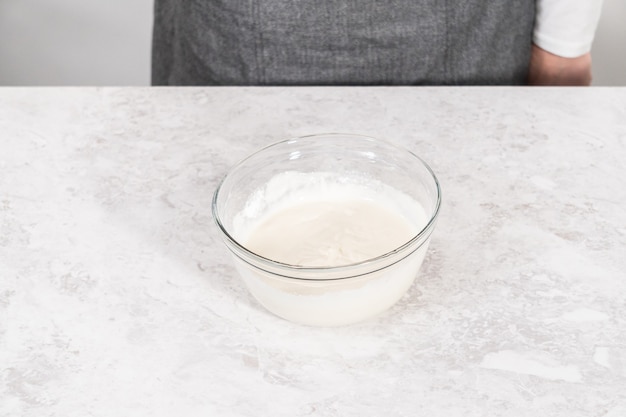 Mixing ingredients in a glass mixing bowl to prepare cream cheese frosting.