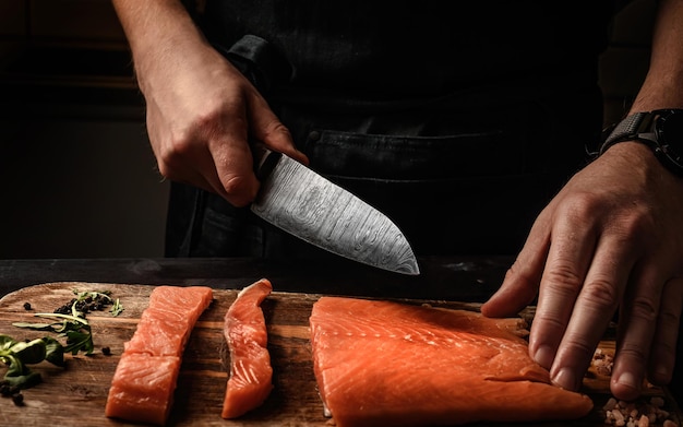 Mle cutting red salmon fish on a cutting board with a big kitchen knife