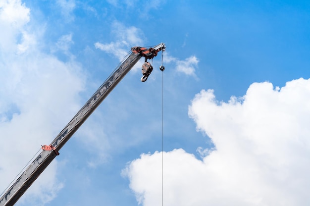 Mobile crane boom with hook hanging by wire cable background blue skyclose up