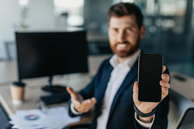 Mobile offer Businessman showing blank smartphone while sitting at desk in office interior selective focus mockup