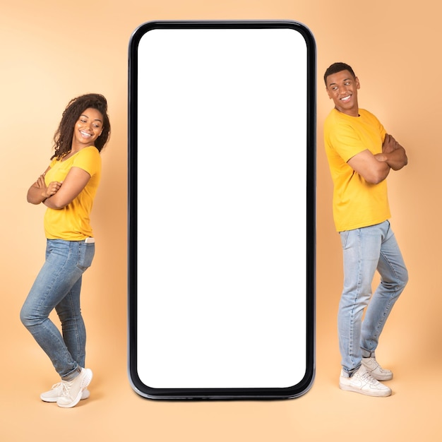 Mobile offer Young black couple looking at giant smartphone with blank screen for mockup advertising or promoting app