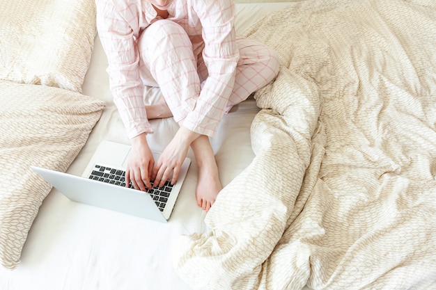 Mobile Office at home. Young woman in pajamas sitting on bed at home working using on laptop pc computer. Lifestyle girl studying indoors. Freelance business quarantine concept.