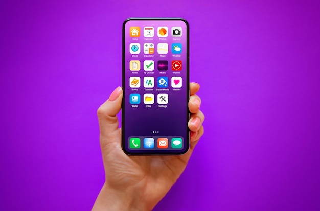 Mobile phone in hand on purple background with sample home screen icons on the screen