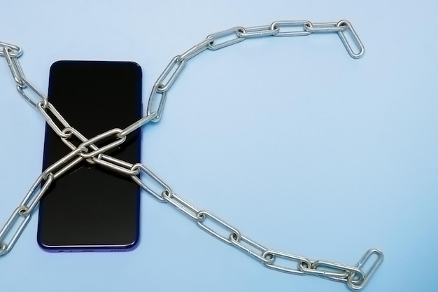 Mobile phone in iron chains on a blue background with copy space