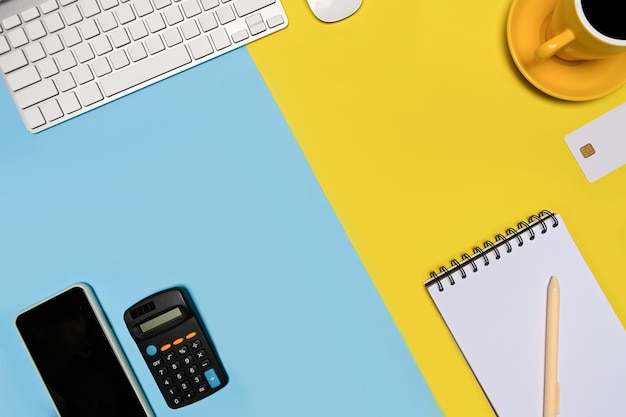 Mobile phone, notepad, coffee cup and calculator on blue and yellow background.