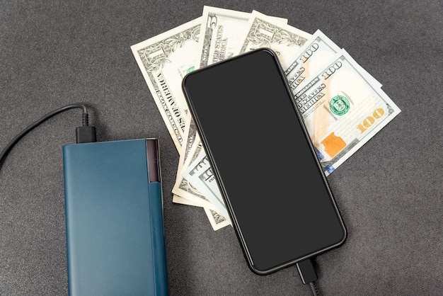 Mobile phone power bank and dollars cash money on grey background Modern technologies save money concept