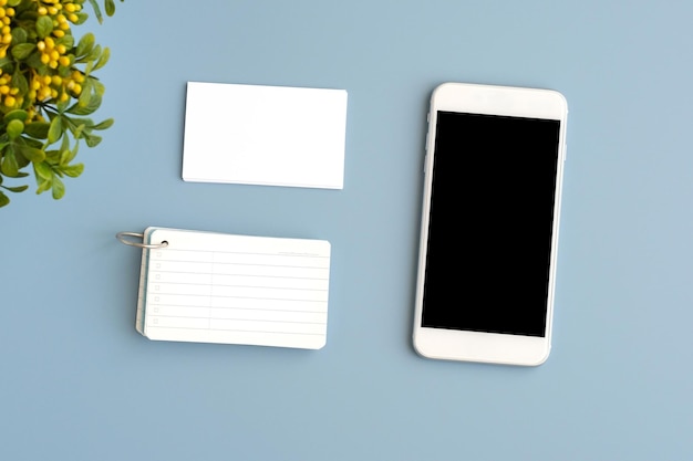 Mobile phone with blank screen and blank business card on gray background