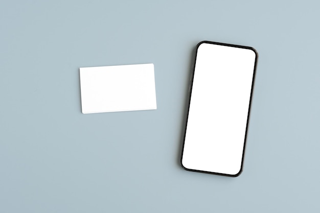 Mobile phone with blank screen and blank business card on gray background