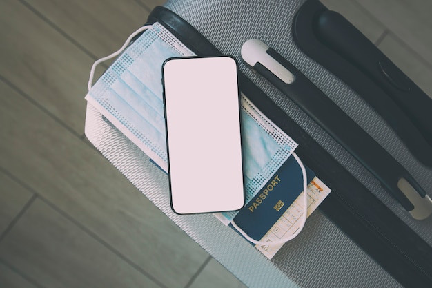 The mobile phone with blank screen for digital vaccination certificate and passport, mask and ticket on the suitcase