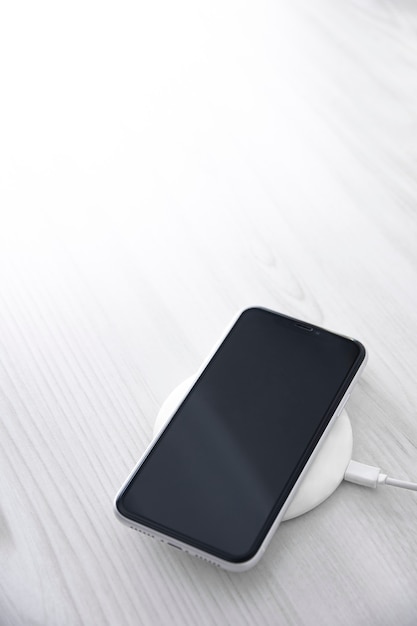 Mobile smart phone on wireless charging device on white background. Icon battery and charging progress lighting on screen.smartphones connected to power source.low battery level problems.Plugged Phone