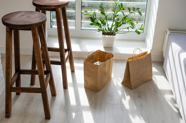 Mock-up of big brown paper package with handles, blank craft shopping bag with area for your logo or design, white wall in the background, food delivery concept