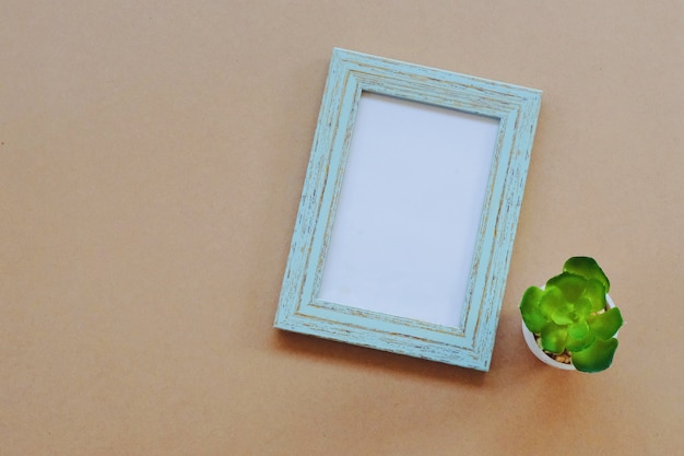 Mock up of blank photo frame with green plant on light brown background