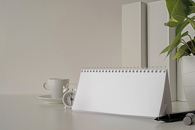 Photo mock up blank spiral calendar with flipping sheets on white table with coffee stationery and clock