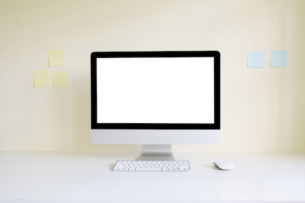 Mock up computer on workspace with empty screen display and sticky note on wall.