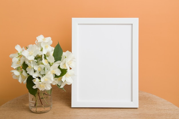 Mock up empty white frame on a round table with jasmine flowers on orange background. Place your text or image