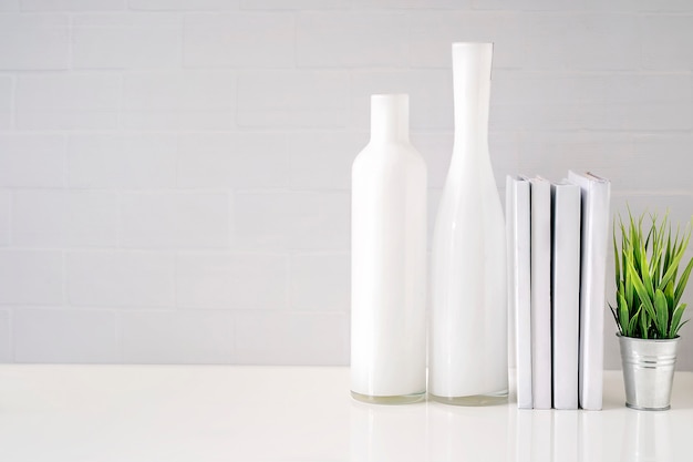 Mock up glass bottle, books and houseplant on white table with white brick wall