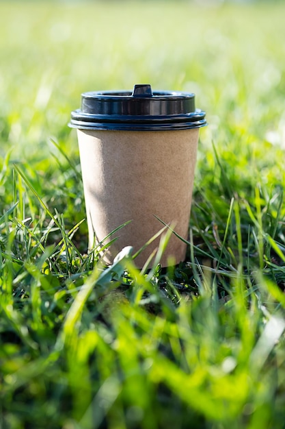 Photo mock up to go coffee cup against green grass disposable craft cardboard takeaway coffee cup