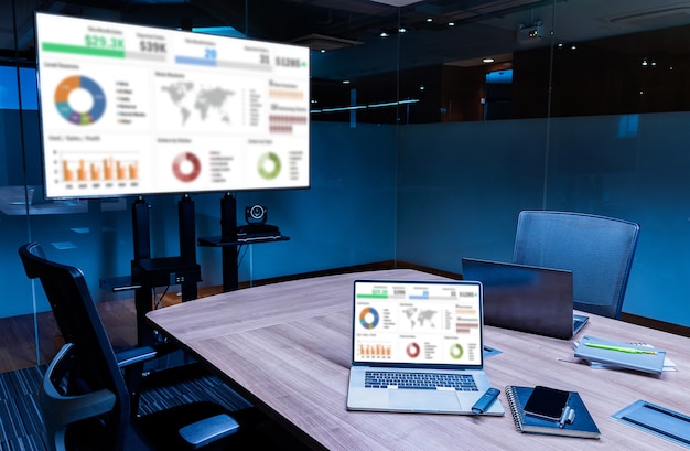 Mock up sales summary slide show presentation on display television and laptop with notebook on table in meeting room