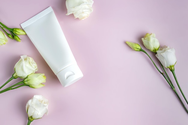 Mock up skincare cosmetic package on pink cosmetic product White cosmetic product in tubes on color background with blooming eustoma flowers Cosmetology skin care cosmetic concept