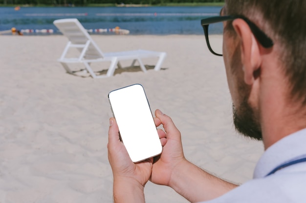 Mock up of a smartphone in the hands of a man on the beach. Against the background of sand and water.