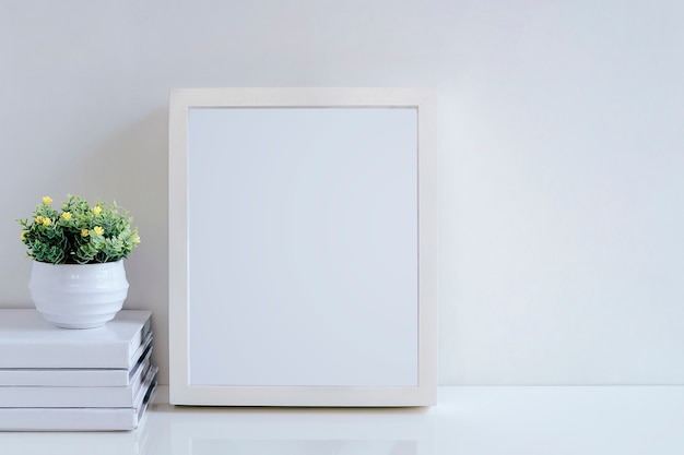 Mock up white wooden frame, books and houseplant on white table