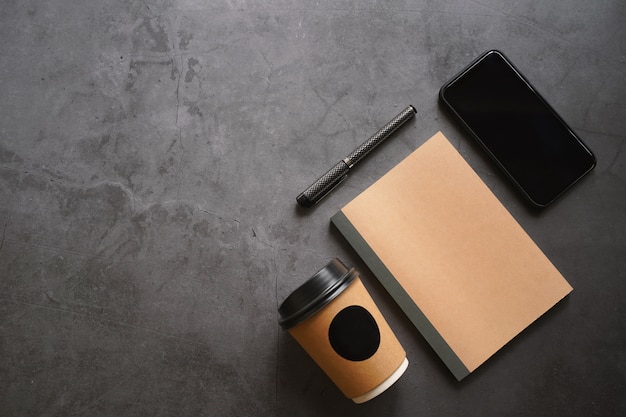 Mock up workspace of smartphone, notebook, take away coffee and pen on dark stone table