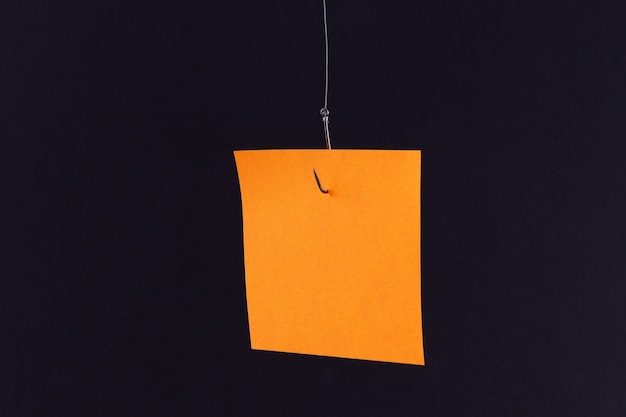 Mockup of a blank orange memo paper with copy space hanging on a fishing hook