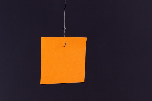 Mockup of a blank orange memo paper with copy space hanging on a fishing hook