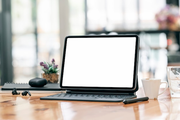 Mockup blank screen tablet with keyboard on wooden table in cafe room.