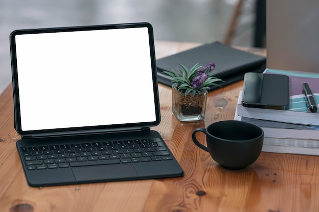 Mockup blank white screen tablet with magic keyboard and supplies on wooden table.