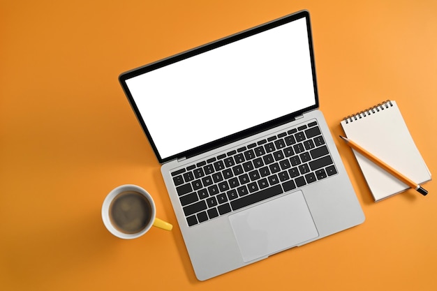 Mockup computer laptop with empty scree coffee cup and notepad on yellow background Top view