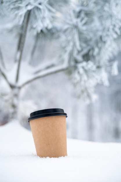 Mockup of a cup of coffee in a snowy winter forest. Logo concept on an empty paper cup, close-up