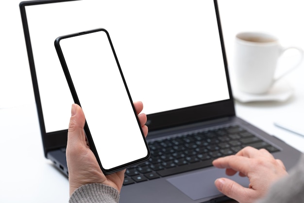 Mockup device businesswoman using smartphone and notebook female hands typing on laptop keyboard with blank white screen cell phone and laptop use at same time