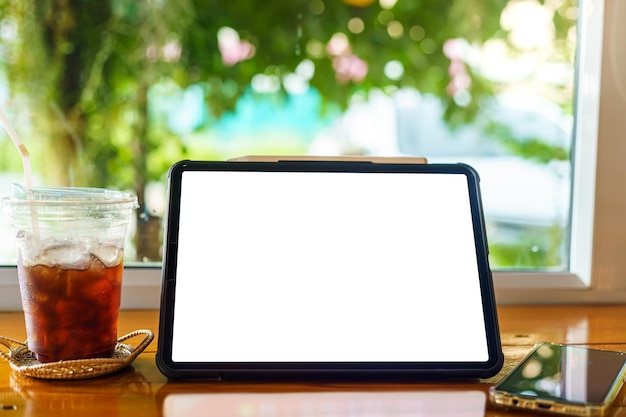 Mockup of digital tablet with empty screen with coffee and smartphone isolate on wooden office desk in coffee shop like the background White screen