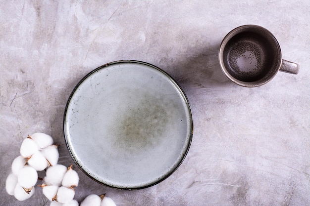 Mockup of empty ceramic plate cup and cotton branch on gray background top view