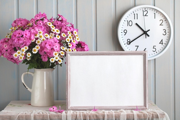 A mockup of an empty frame and a bouquet of garden flowers on the table Phlox and daisies