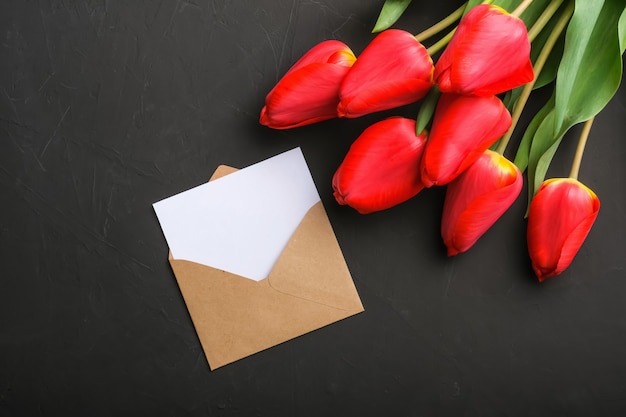 Mockup of fresh red tulips bouquet and blank greeting card in kraft envelope