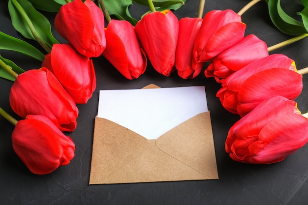 Mockup of fresh red tulips bouquet and blank greeting card in kraft envelope