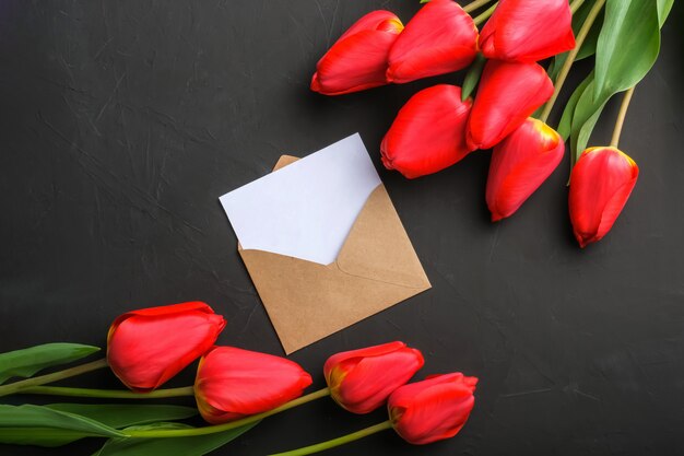 Mockup of fresh red tulips bouquet and empty greeting card in kraft envelope