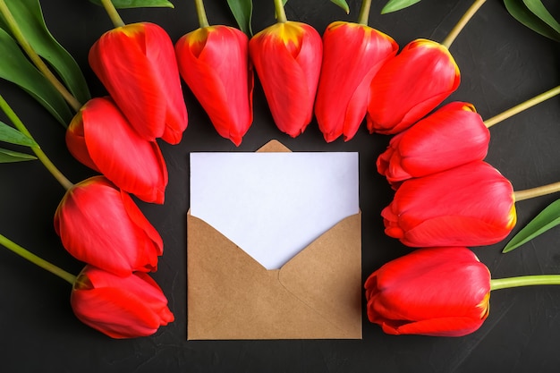 Mockup of fresh red tulips bouquet and greeting card in kraft envelope