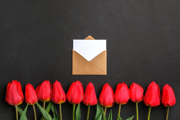 Mockup of fresh red tulips bouquet in the row and greeting card in kraft envelope