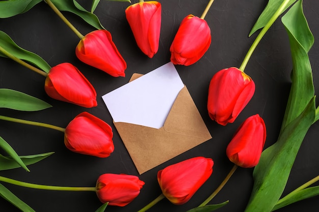 Mockup of fresh red tulips bouquet and white blank greeting card in kraft envelope