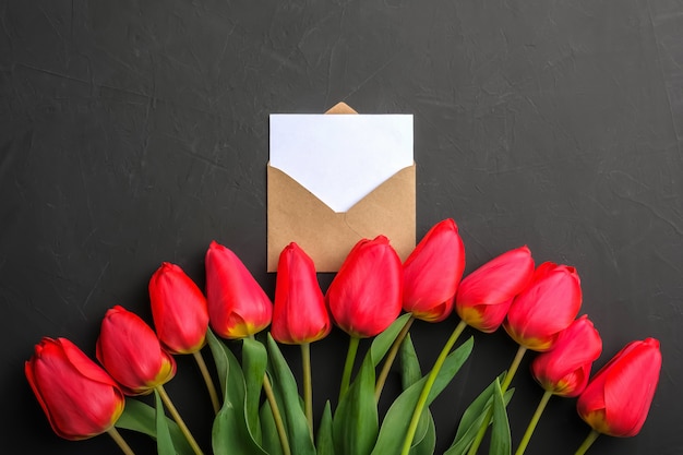 Mockup of fresh red tulips bouquet and white empty greeting card in kraft envelope