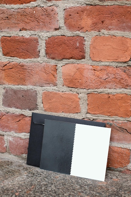 Mockup friendly vertical template of postcard certificate with black envelope on a brick wall