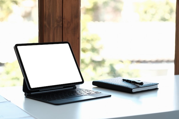 mockup image of black digital tablet pc with blank desktop white screen on working space at home office.