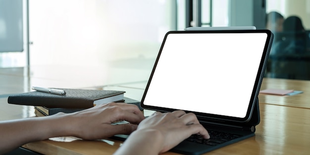 Mockup image of business woman using and typing on laptop with blank white screen and coffee cup on glass table in modern loft cafe