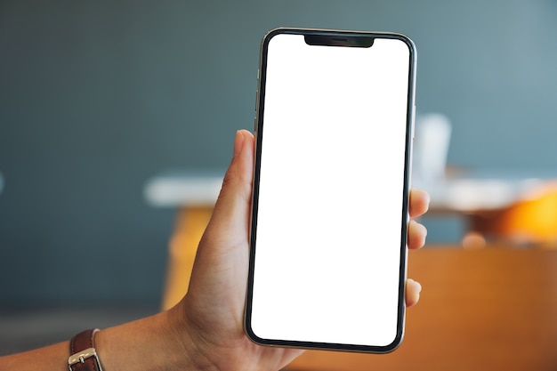 Mockup image of a hand holding and showing black mobile phone with blank screen in cafe