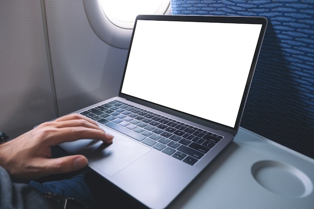 Mockup image of a man using and touching on laptop computer touchpad with blank white desktop screen while sitting in the cabin